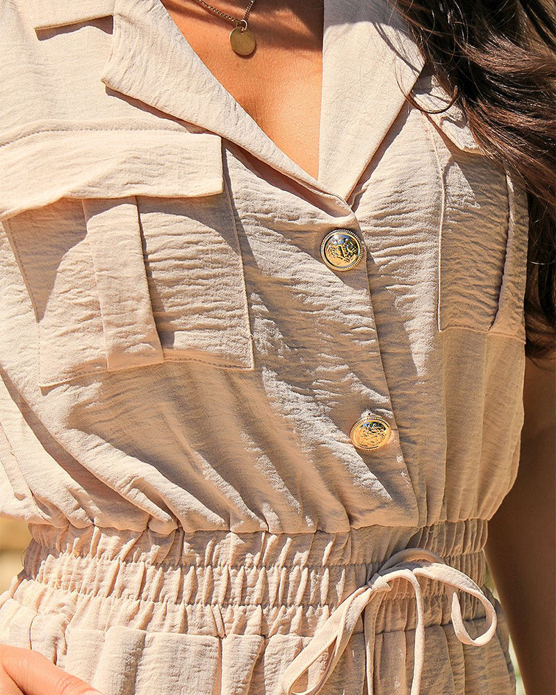 Light beige sleeveless notched collar jumpsuit with drawstring waist, flap pockets, and gold buttons.