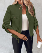 Olive green roll tab sleeve zip jacket with drawstring hem, worn over white top and black pants.