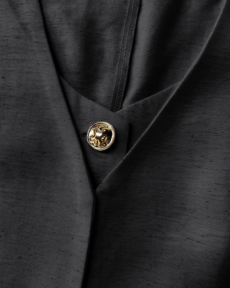 Black suit jacket with textured fabric and single gold lion-embossed button in close-up.
