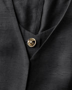 Black suit jacket with textured fabric and single gold lion-embossed button in close-up.