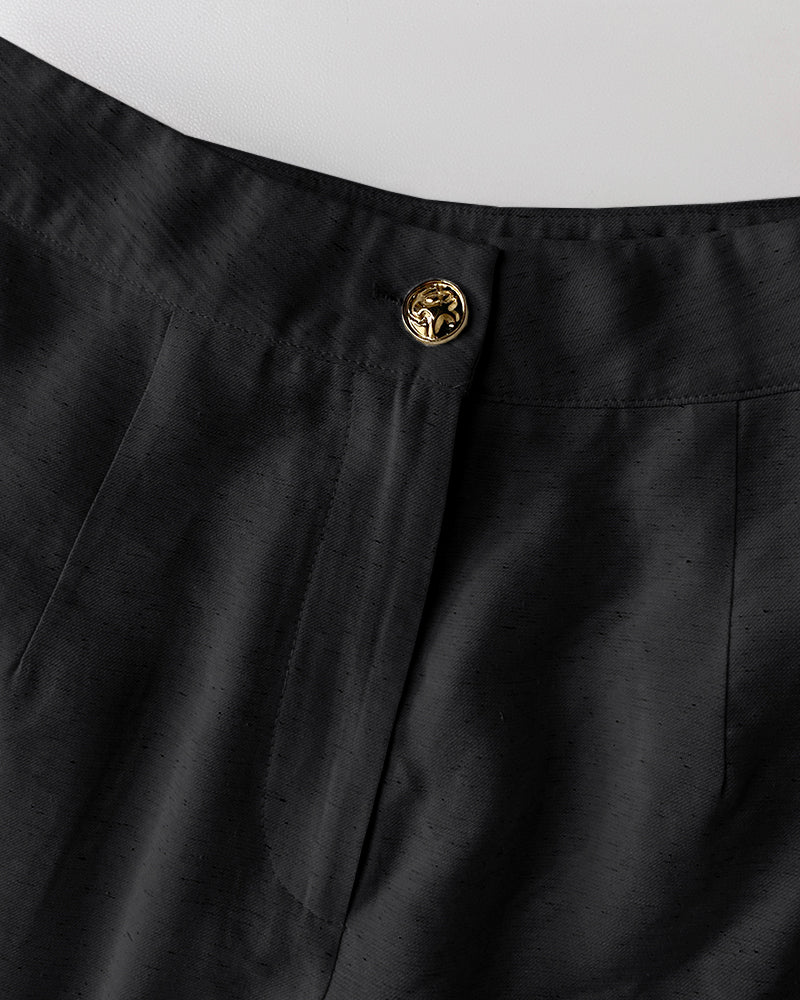 Black V-neck vest crop top and wide-leg pants with lion’s head gold button waistband.