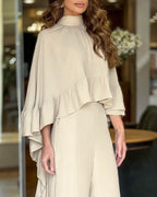 A high neck cape with ruffled sleeves and neckline, paired with wide-leg pants.
