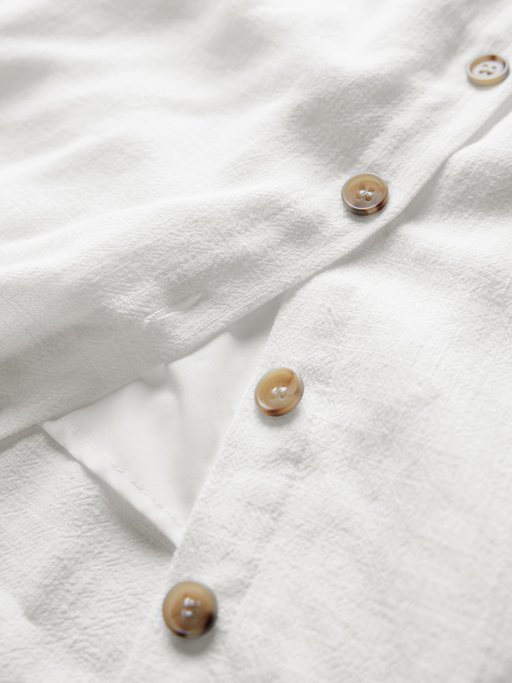 White textured linen mini dress with brown buttons and a visible side pocket detail.