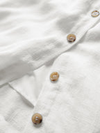 White textured linen mini dress with brown buttons and a visible side pocket detail.
