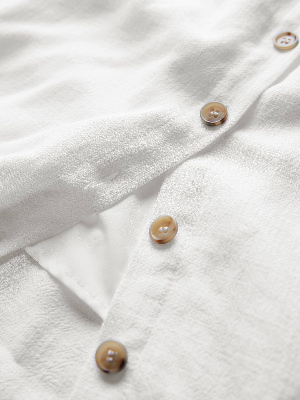 White textured linen mini dress with brown buttons and a visible side pocket detail.