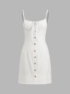 White sleeveless linen mini dress with thin straps, gathered bust tie, and brown buttons.