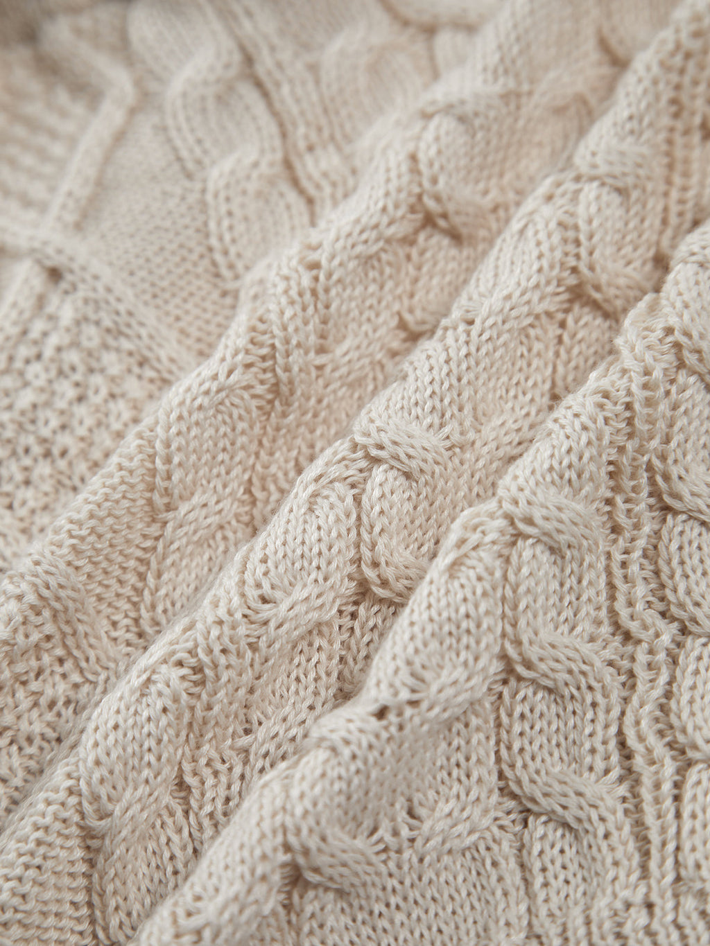 Cream-colored, sleeveless cable knit halter crop with drawstring and textured interwoven details.