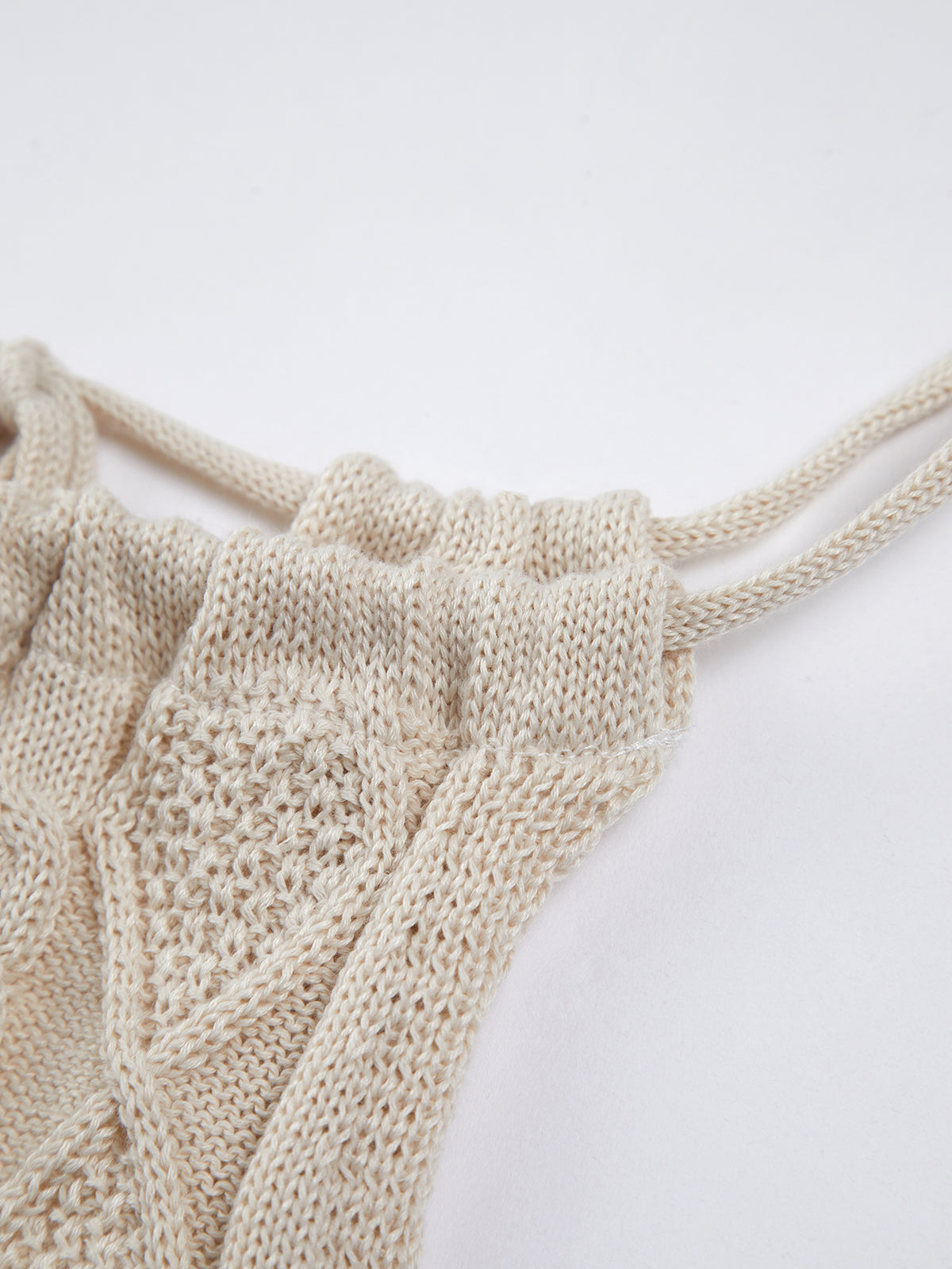 A cream cable knit halter crop top with open back and twisted drawstring details.