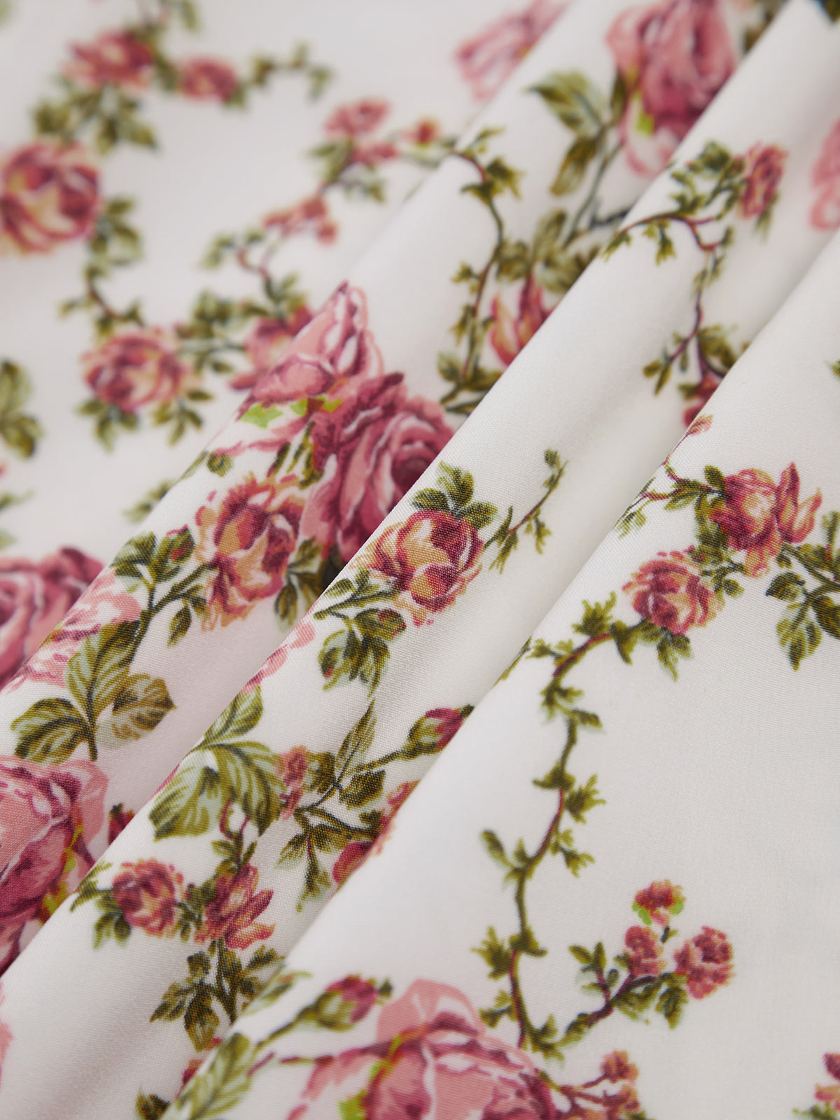 White midi dress with pink and green blooming roses, leafy accents, and a soft texture.
