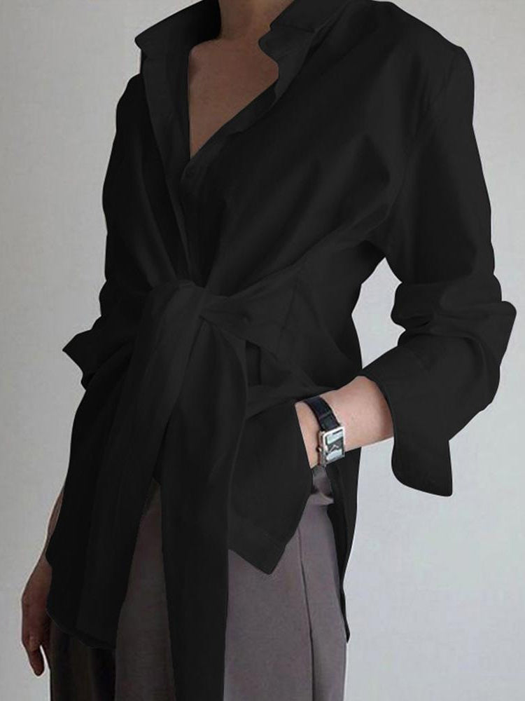 Black, belted, long-sleeve semi-sheer blouse with button-down ties, paired with dark pants.