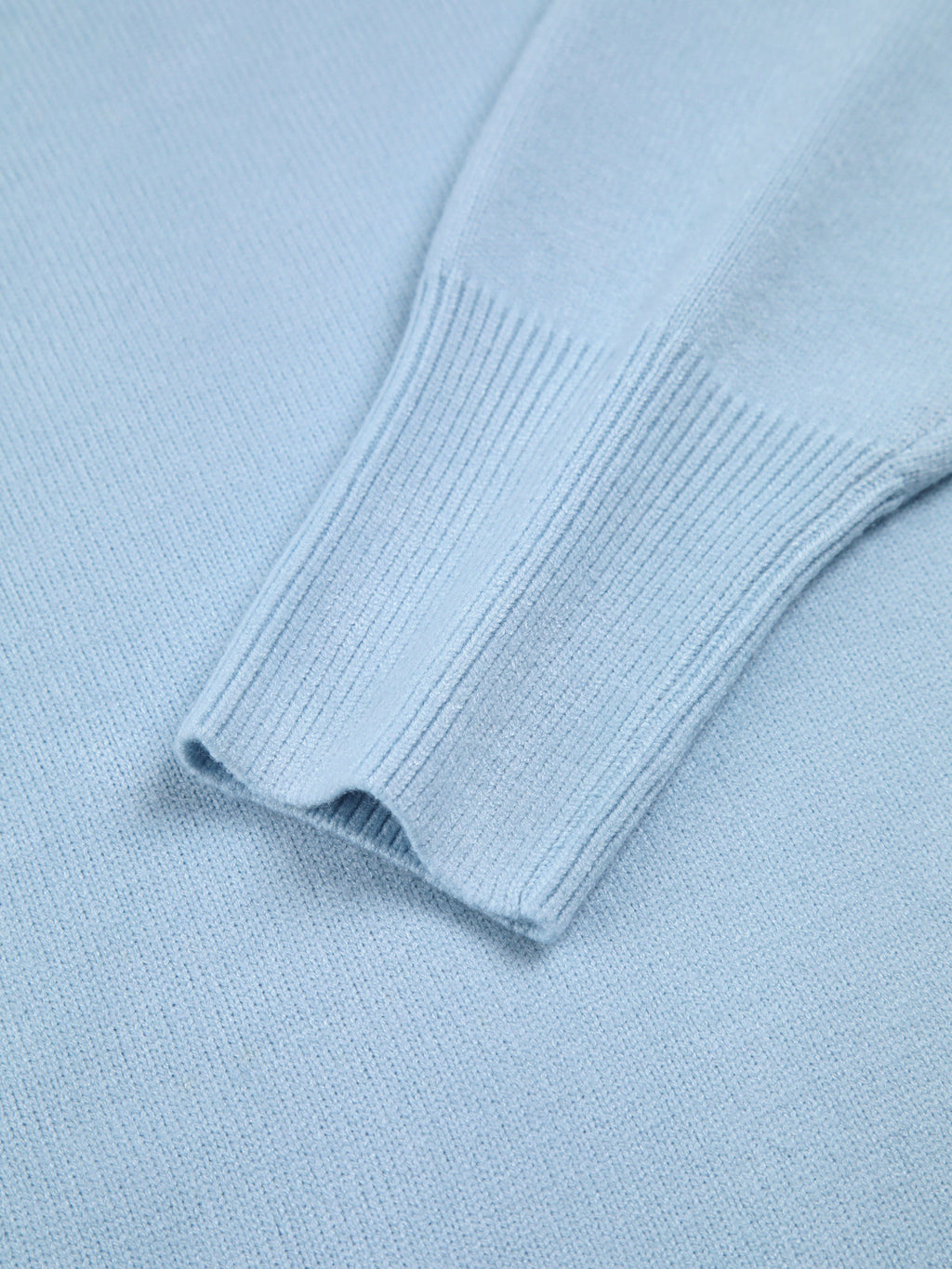 Close-up of blue turtleneck sweater sleeve, showing ribbed cuff and smooth knit fabric.