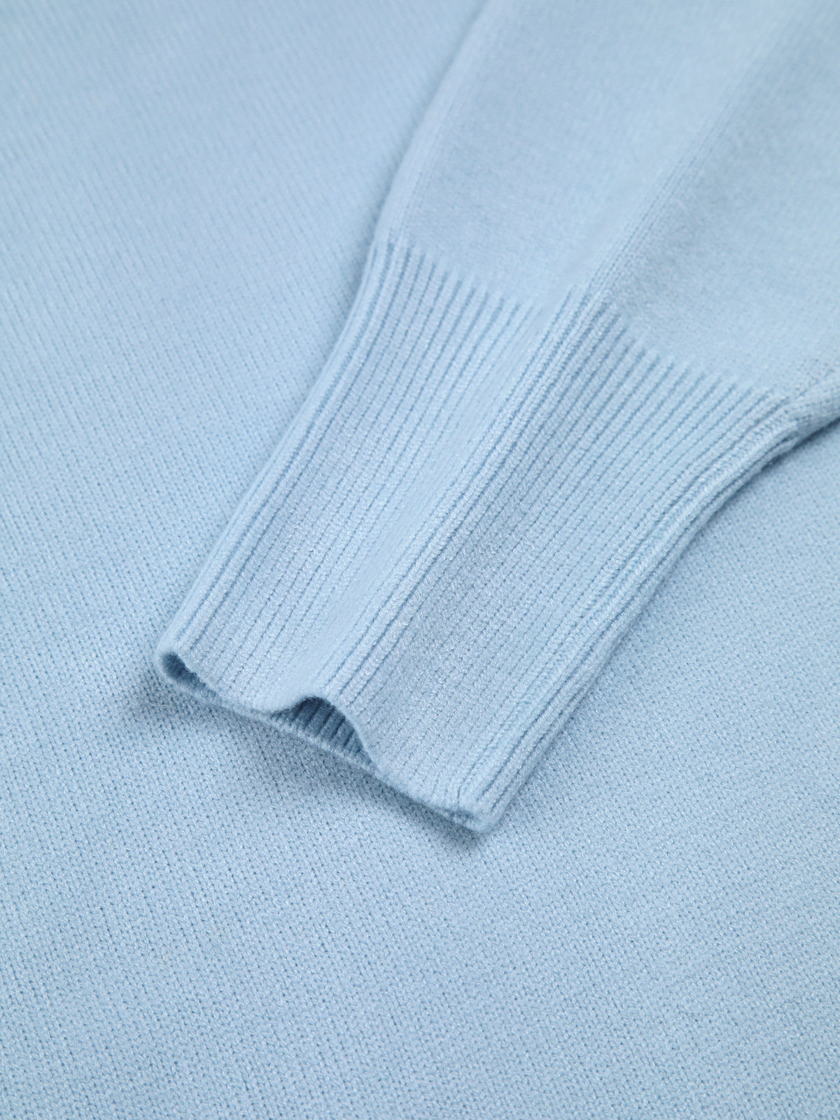 Close-up of blue turtleneck sweater sleeve, showing ribbed cuff and smooth knit fabric.