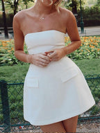 Sleek white tube top mini dress with a woven texture and two decorative pocket flaps.