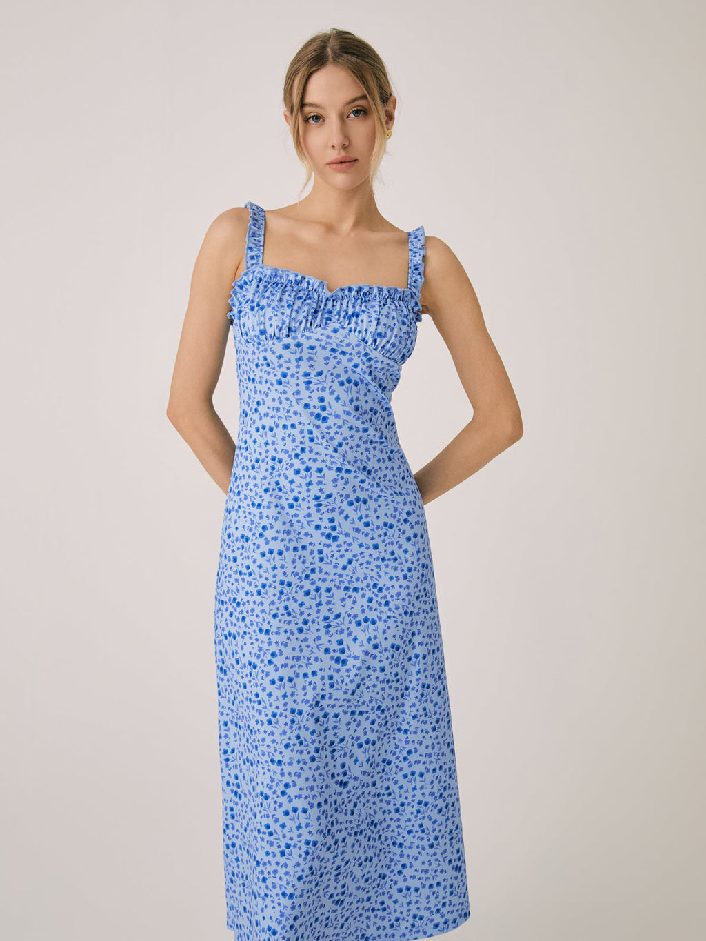 Light blue, sleeveless slim-fit midi dress with ruffled neckline and dark blue floral pattern.