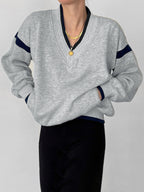 Light gray oversized V-neck sweatshirt with navy sleeve stripes, paired with black pants.