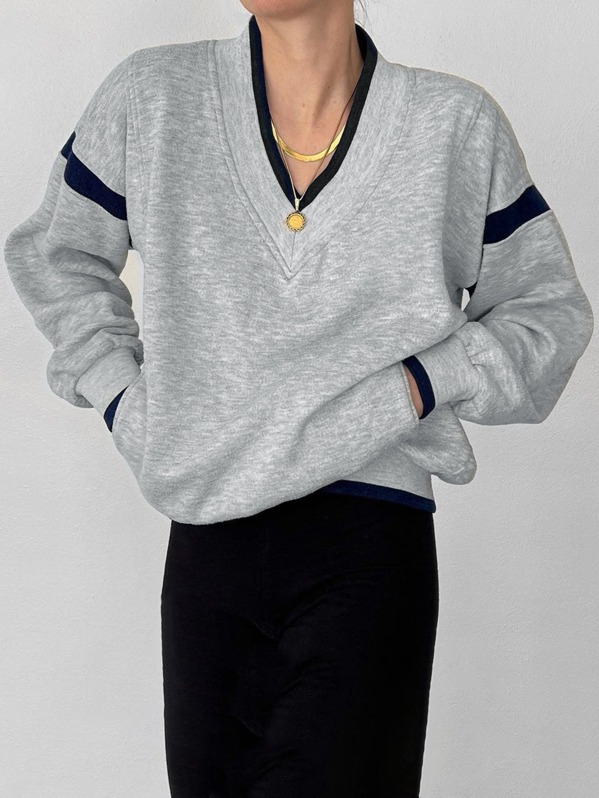 Light gray oversized V-neck sweatshirt with navy sleeve stripes, paired with black pants.
