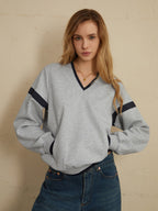 Light gray oversized sweatshirt with navy sleeve stripes, paired with classic blue jeans.