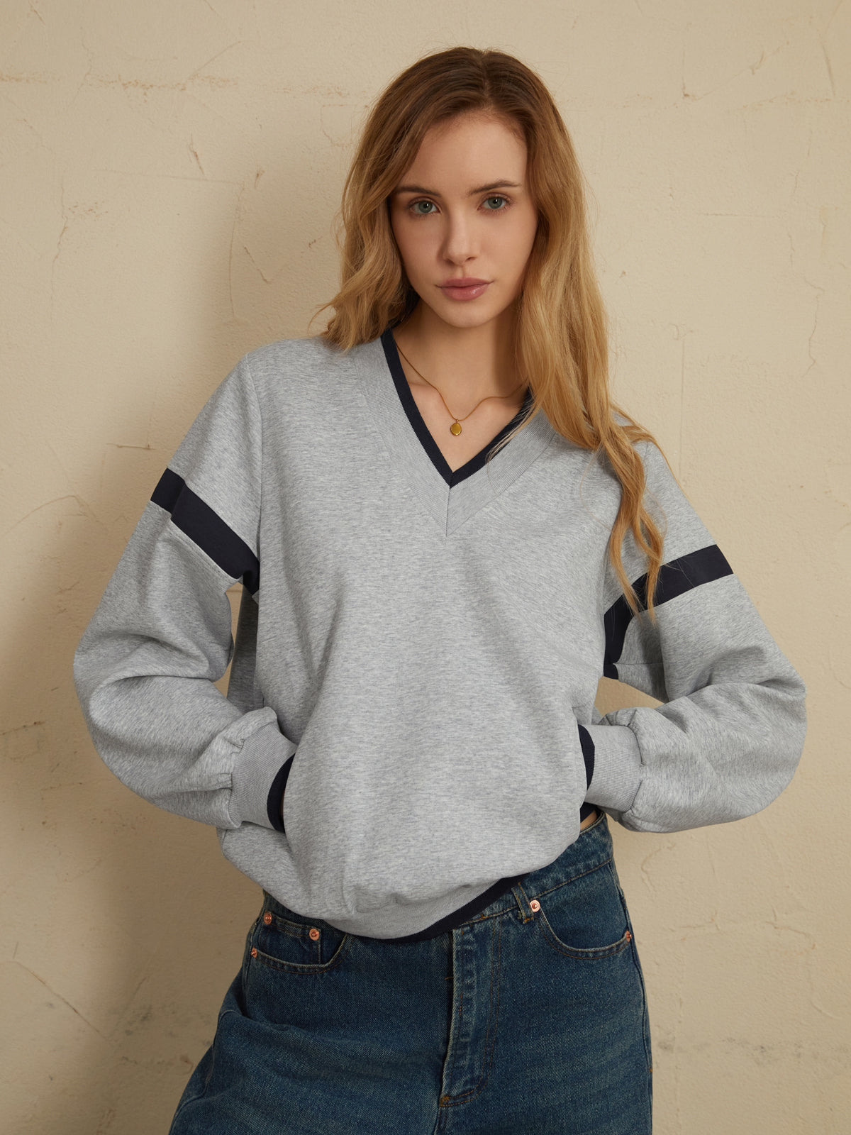 Light gray oversized sweatshirt with navy sleeve stripes, paired with classic blue jeans.