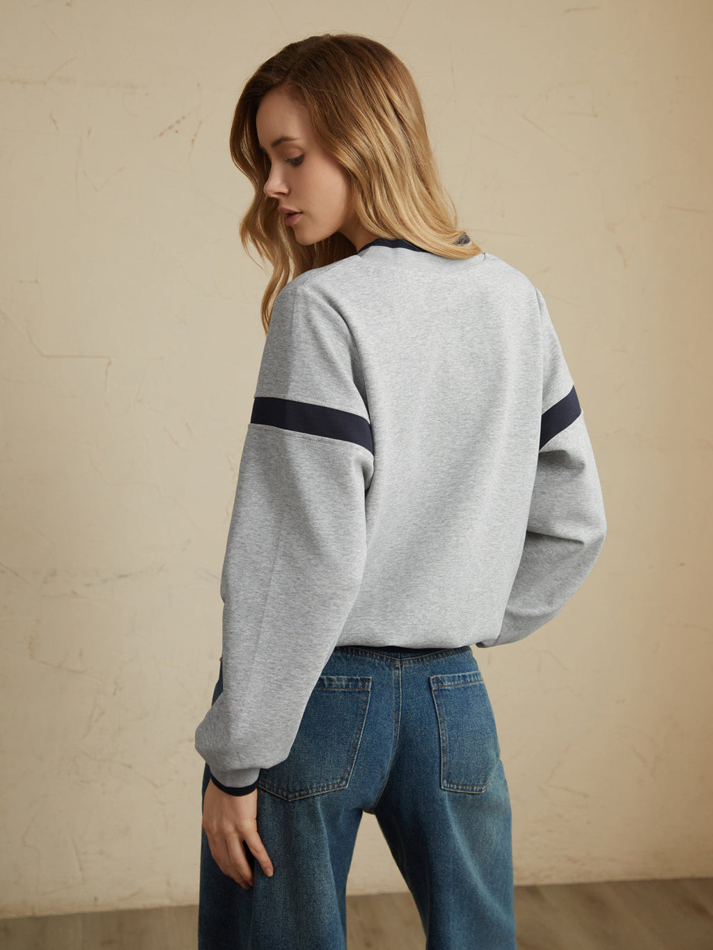 Light gray oversized sweatshirt with dark sleeve stripes, paired with classic blue jeans.