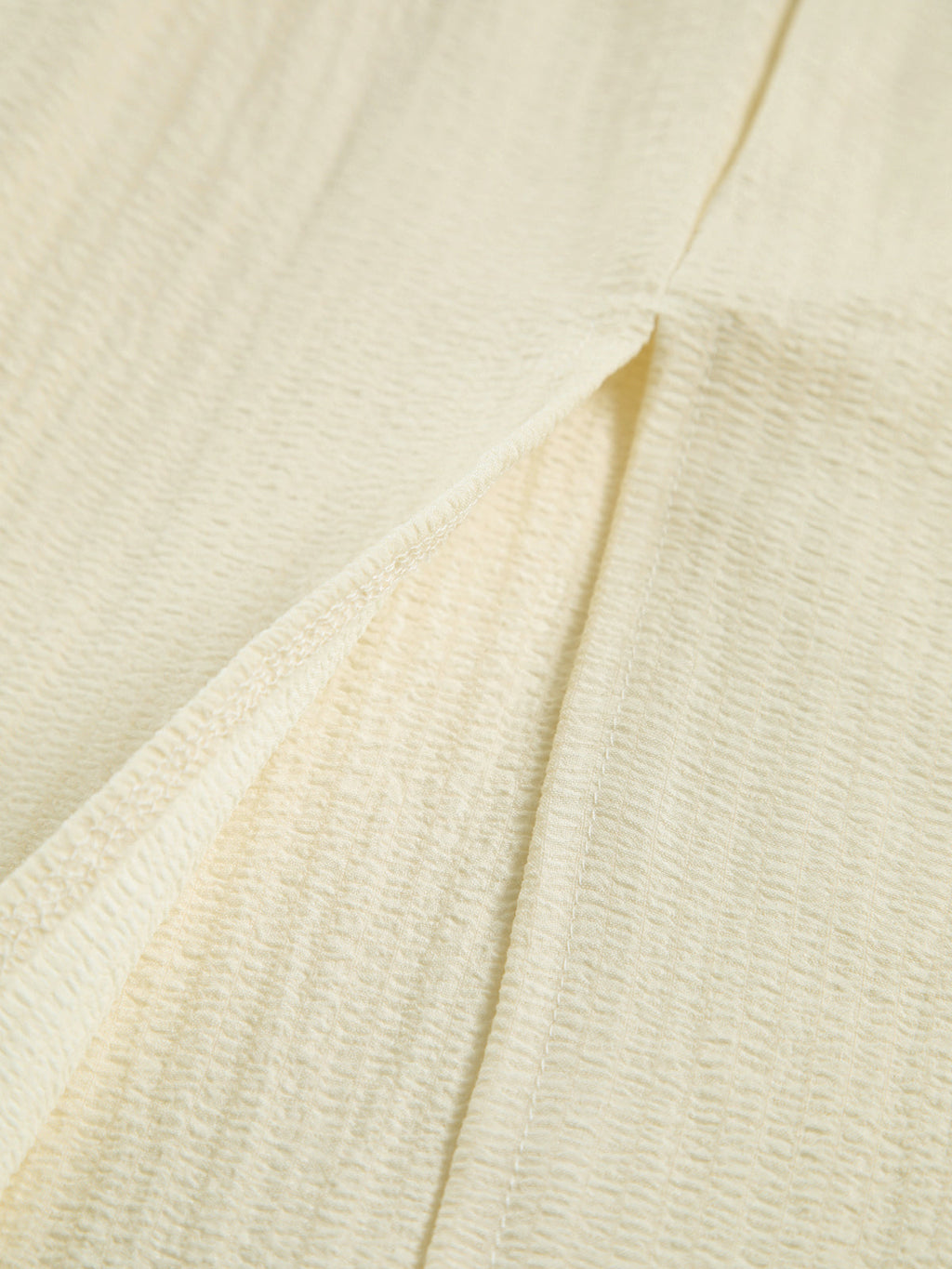 Cream-colored textured dress fabric with crinkled pattern and visible seam stitching details.