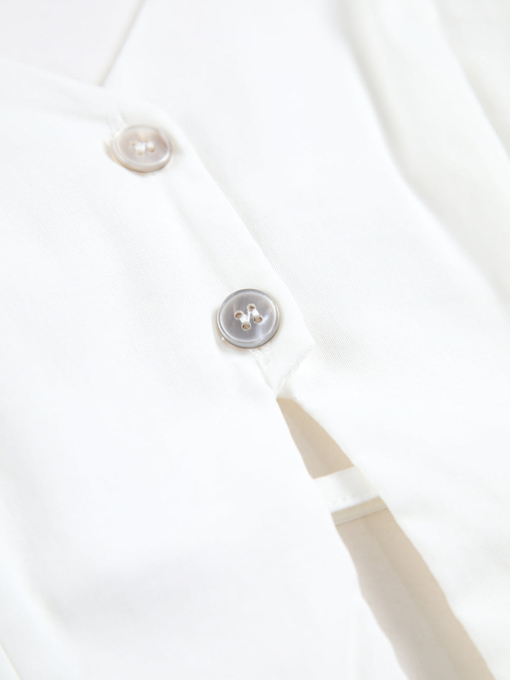 White backless halter neck camisole top with two light buttons, smooth fabric, refined stitching.