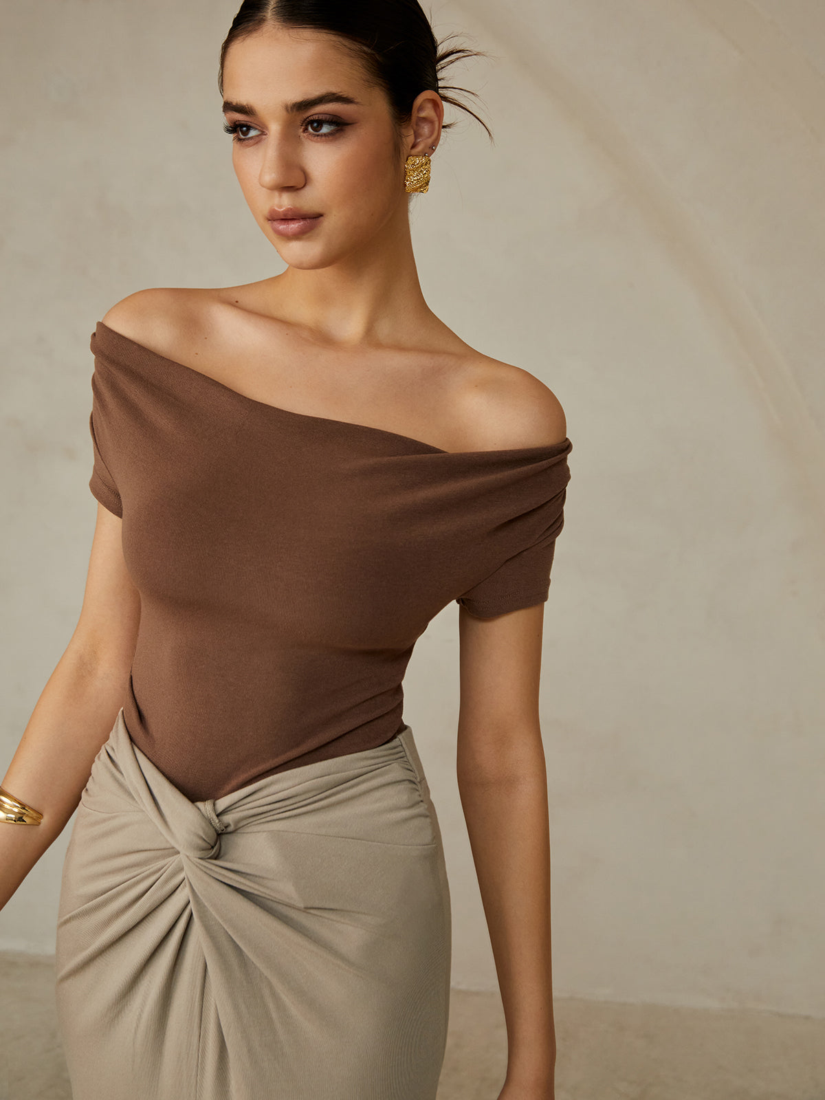 A brown pleated off-shoulder tee paired with a beige knotted skirt.