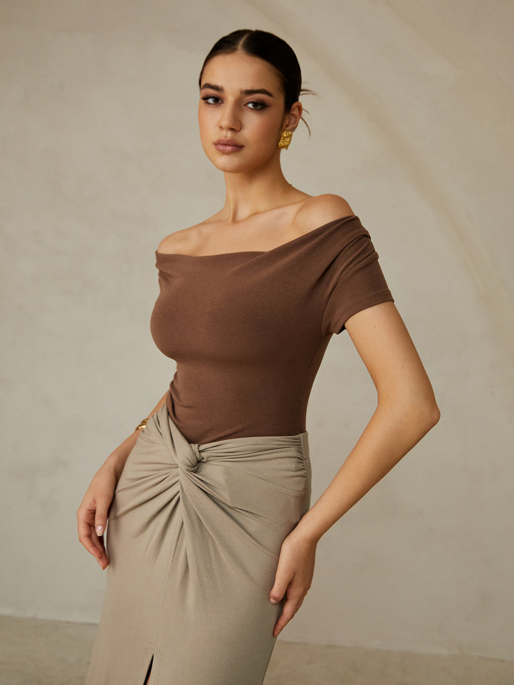 A brown off-shoulder pleated tee paired with a beige gathered-knot skirt.