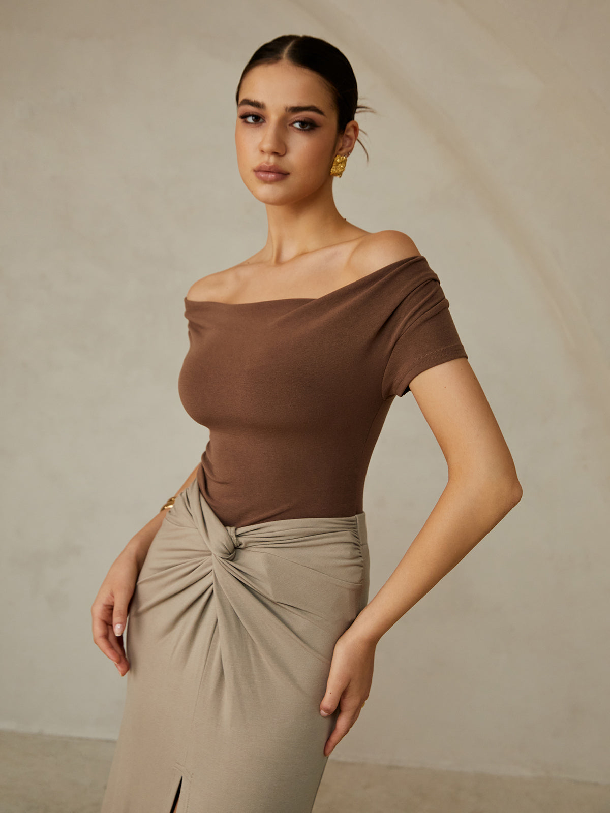 A brown off-shoulder pleated tee paired with a beige gathered-knot skirt.