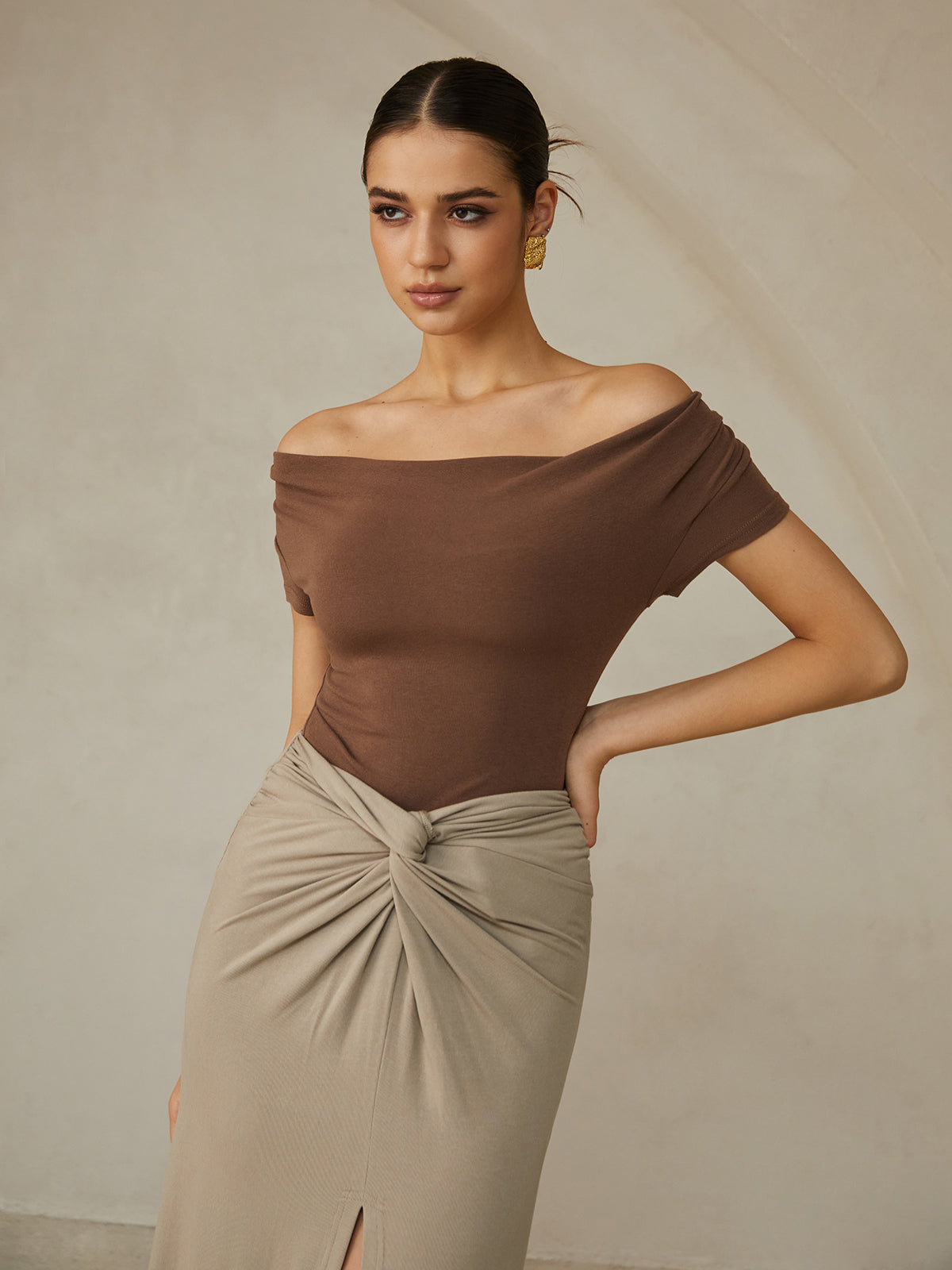 A brown pleated off-shoulder tee paired with a beige knotted skirt.