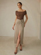 Brown off-shoulder pleated tee paired with a beige high-waisted skirt featuring a slit.