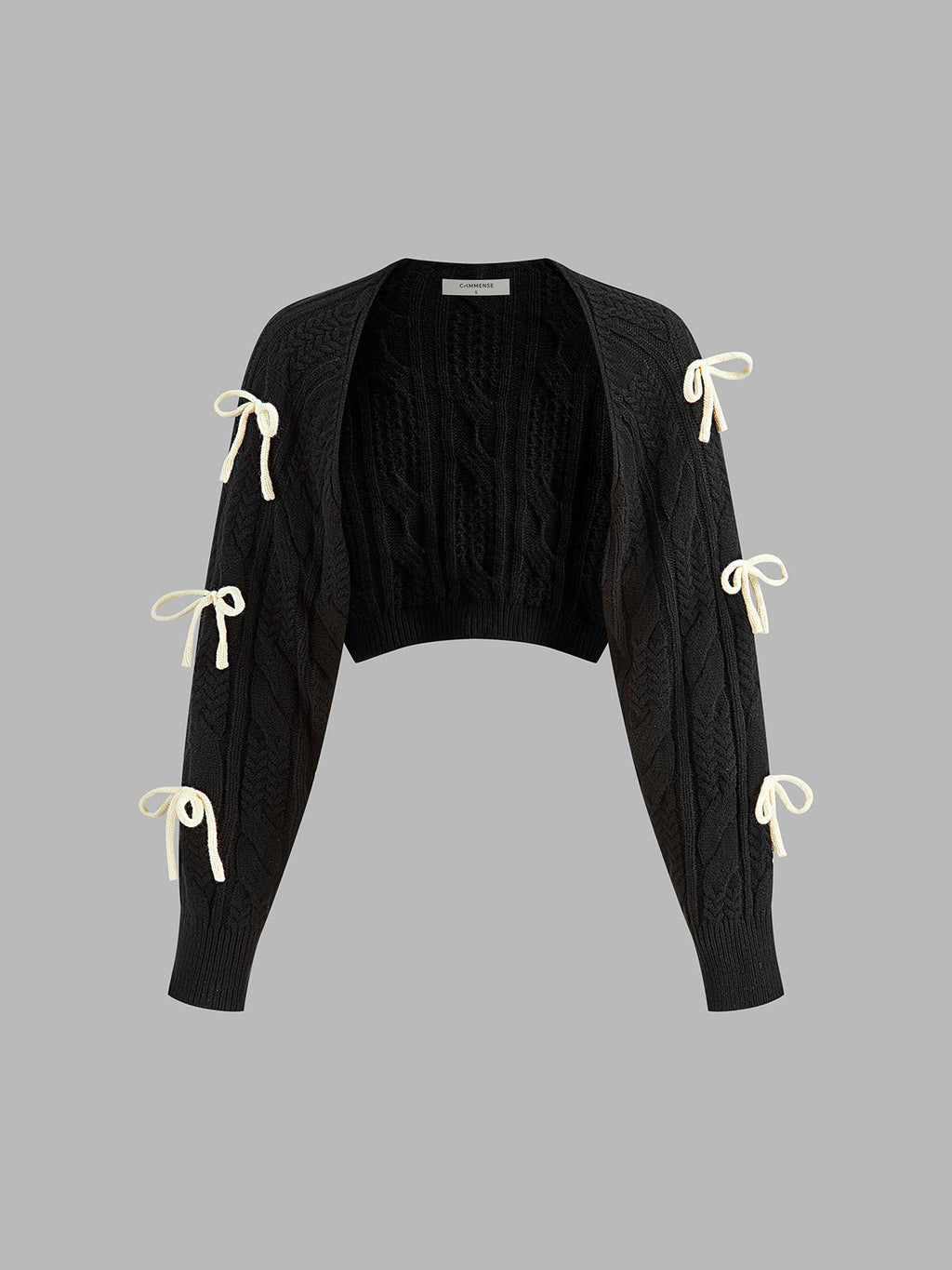 Black cropped cable knit cardigan with long sleeves and six cream ribbon bow accents.