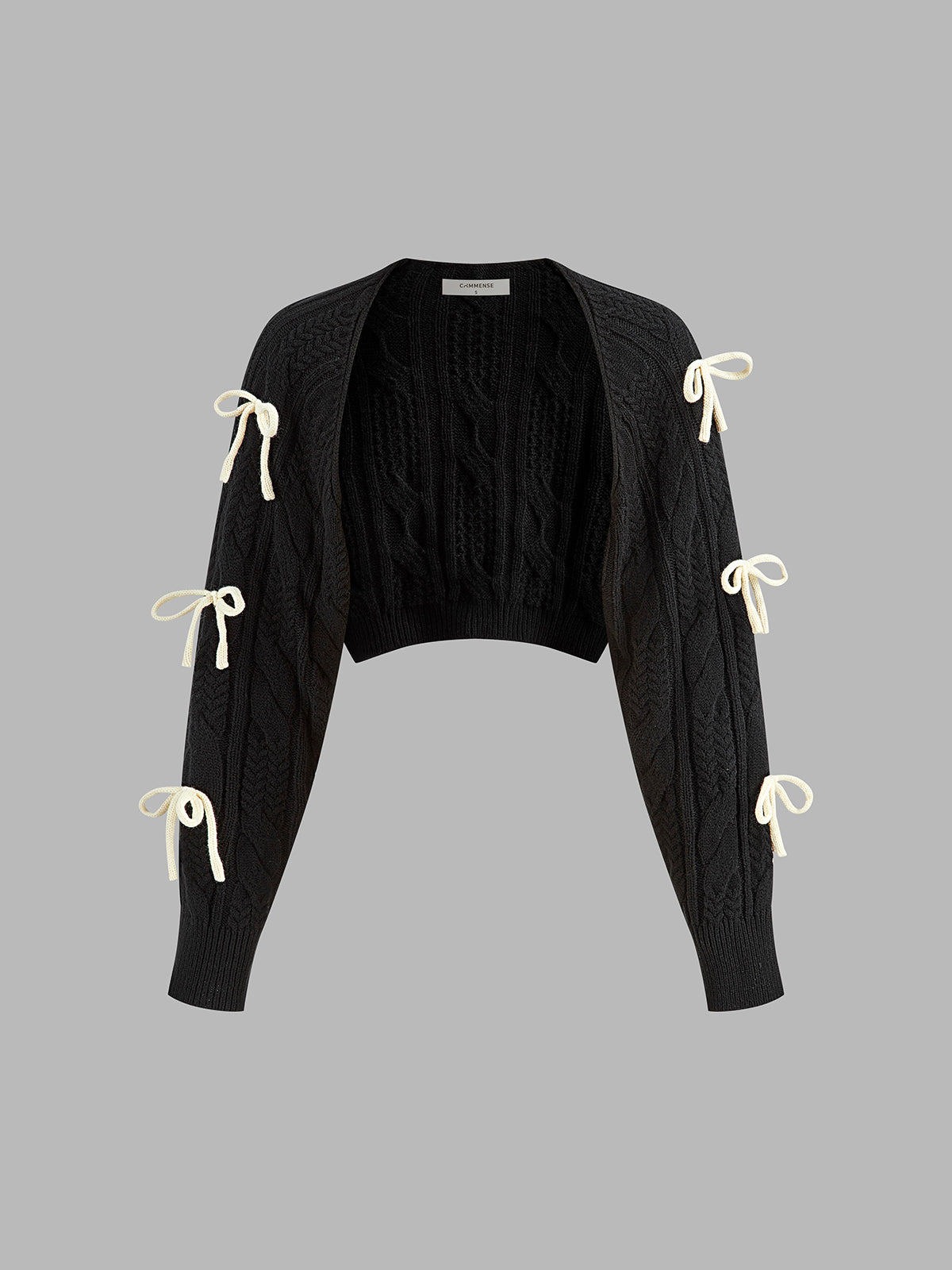 Black cropped cable knit cardigan with long sleeves and six cream ribbon bow accents.