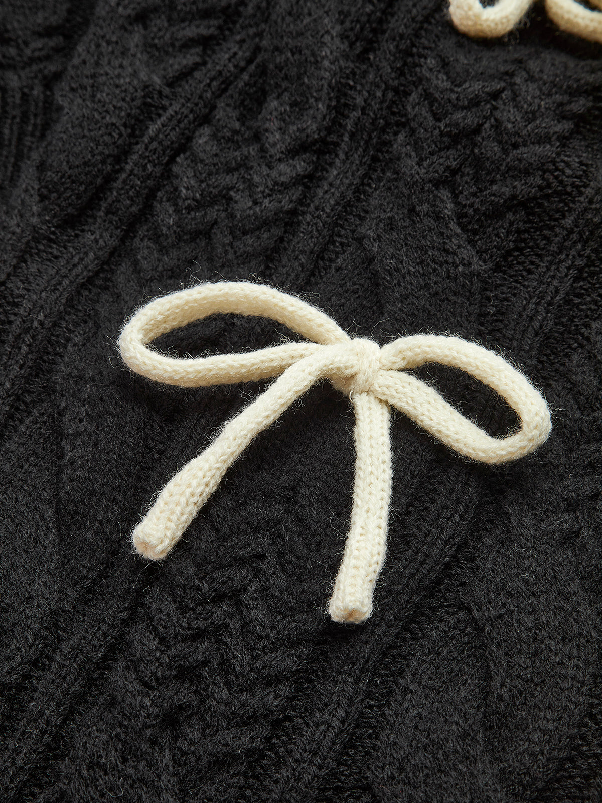 A cable knit cardigan with a cream-colored bow-knot accent and textured black knit pattern.