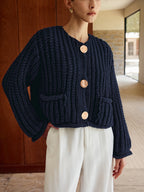 Chunky navy blue button-up cardigan with gold buttons, paired with crisp white trousers.