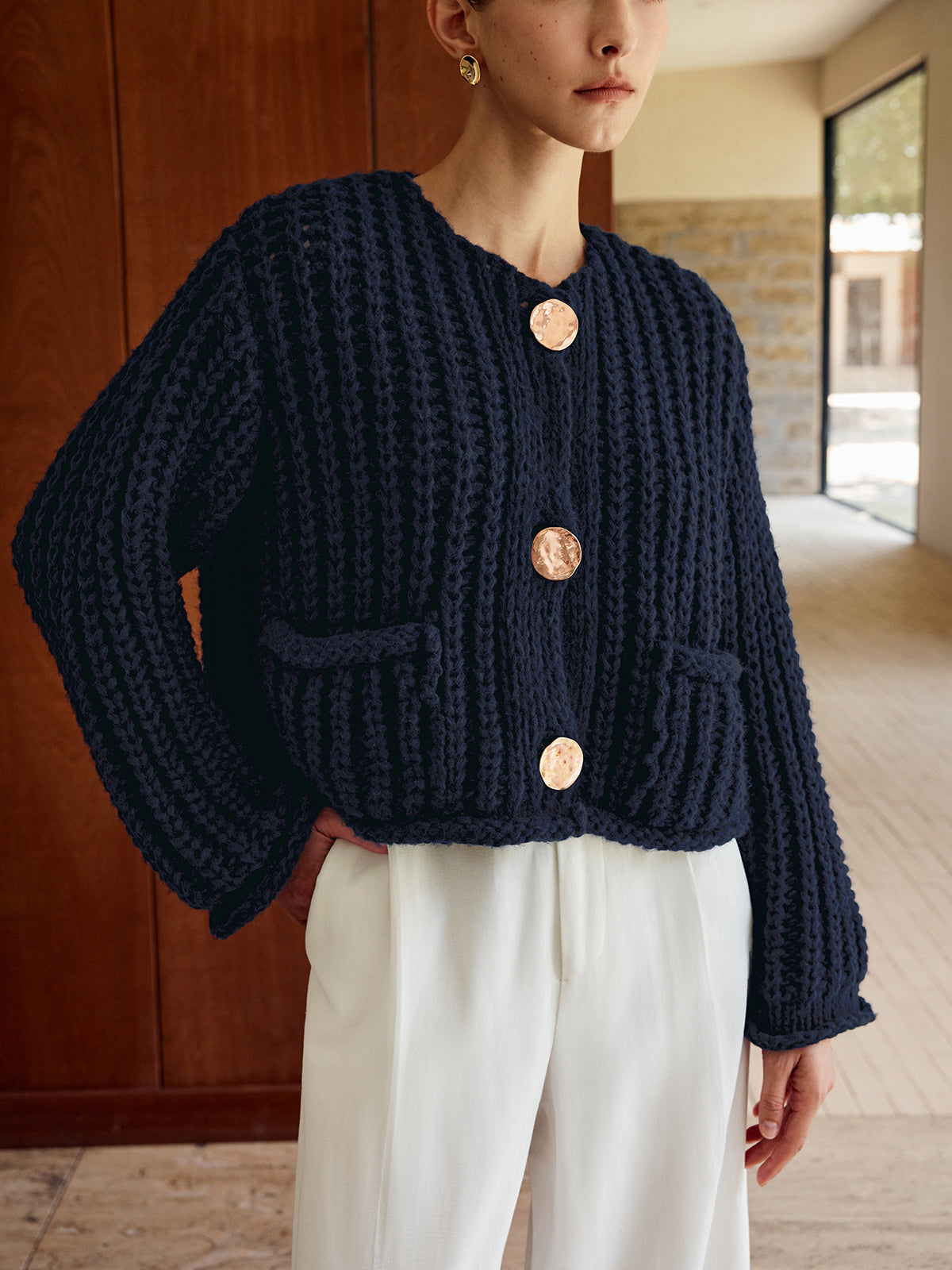 Chunky navy blue button-up cardigan with gold buttons, paired with crisp white trousers.
