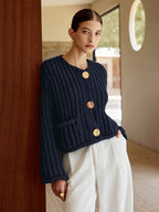 A navy soft knit button-up cardigan with large gold buttons, paired with white pants.
