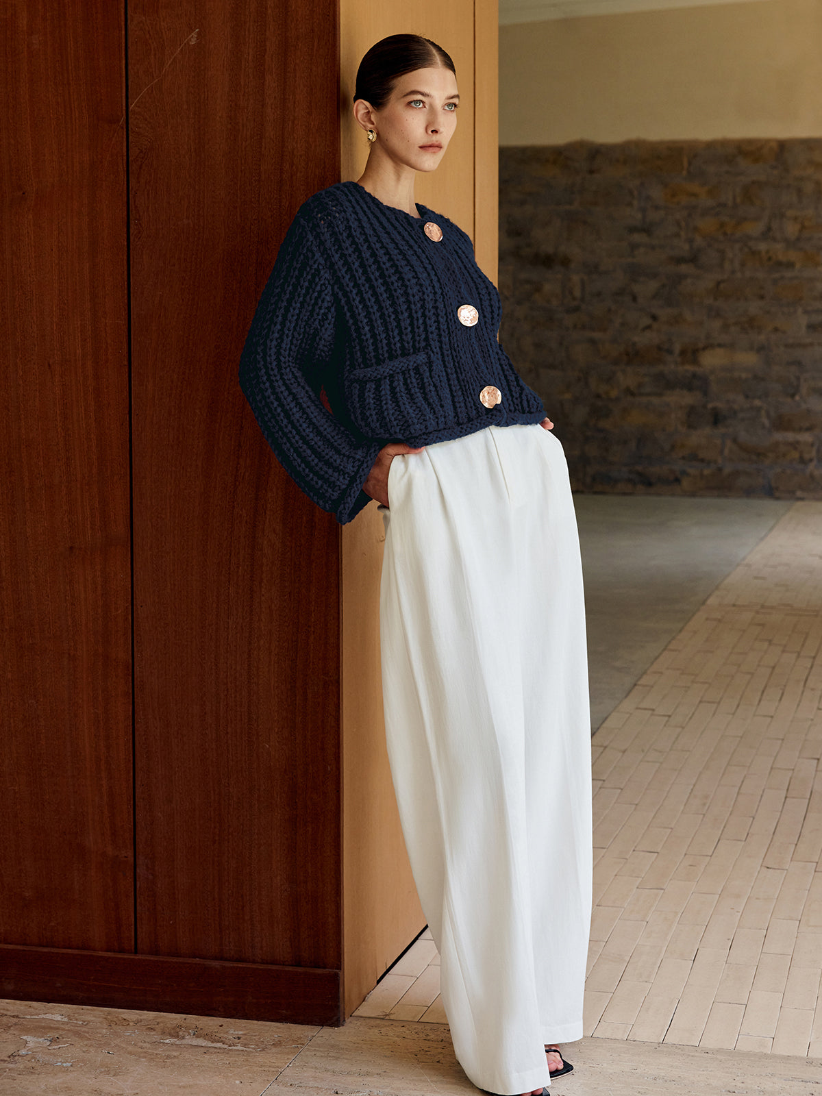 Timeless button-up soft knit cardigan and loose, high-waisted white trousers ensemble.