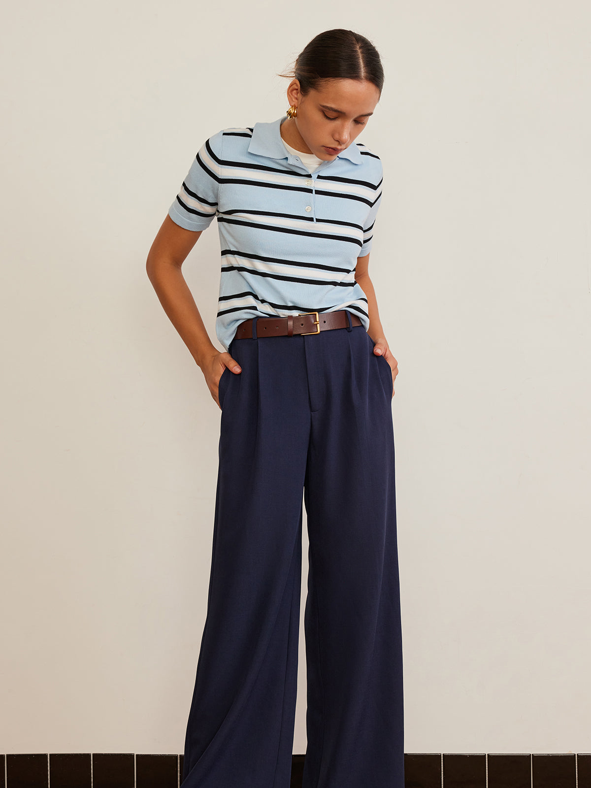 Striped knit top with lapel detail, paired with wide-leg navy trousers and brown belt.