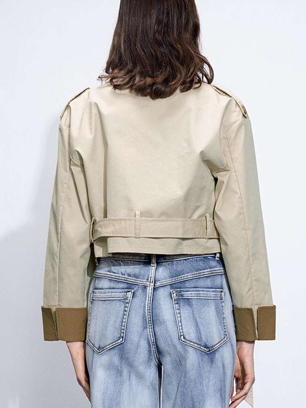 Dual-tone trench coat with beige and olive green sleeves, buckle belt, and light-wash blue jeans.