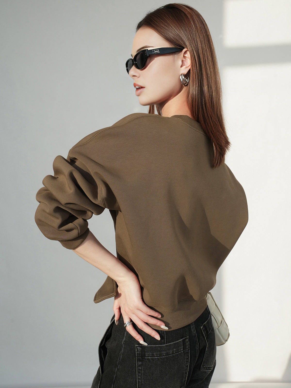A cinched waist, short-length sweatshirt sweater paired with black jeans.