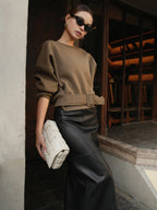 Cinched waist short-length sweatshirt sweater with a belt, paired with a black leather skirt.