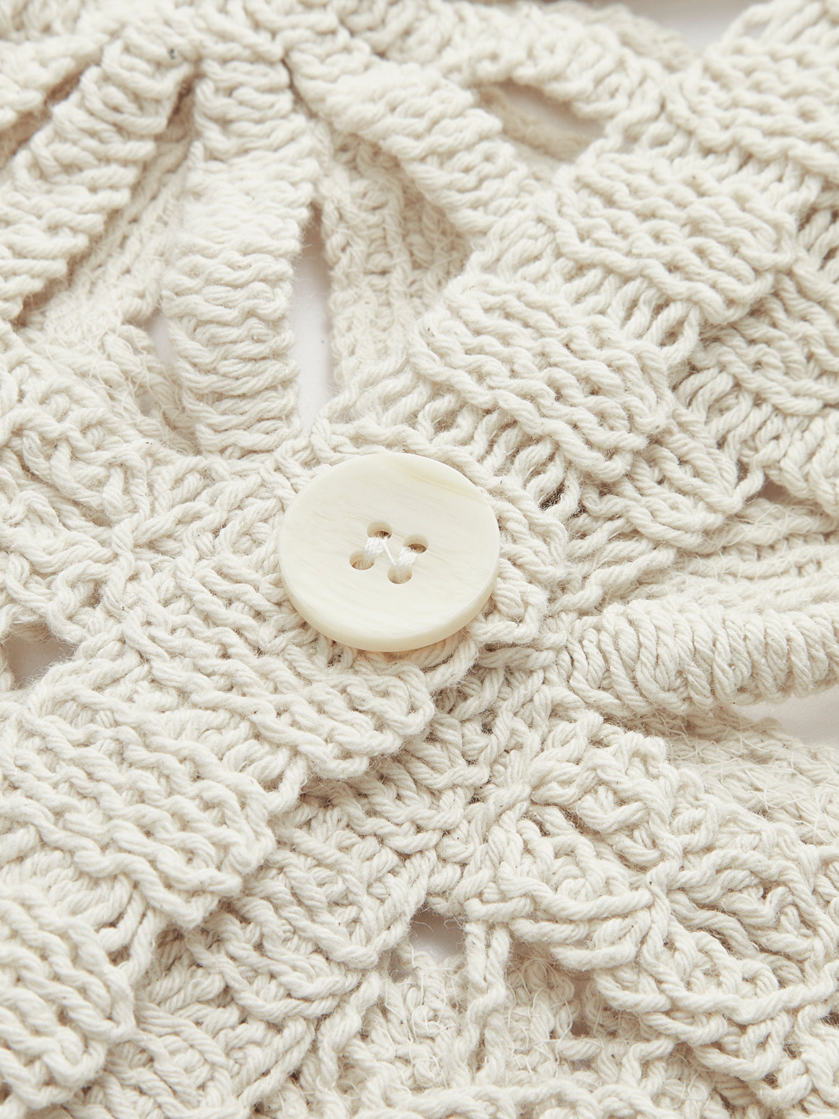Cream crochet button-up sweater with square pattern and central round pearl-like four-hole button.