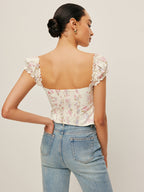 LA FINE FLEUR Tie-Front Bustier Top with ruffled sleeves and light blue high-waisted jeans.