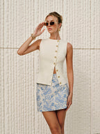 Sleeveless cream top with gold buttons, blue-and-white floral mini skirt, textured knit vest.