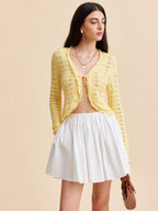 A crocheted cardigan sweater with tie-front design styled over a white flared mini skirt.