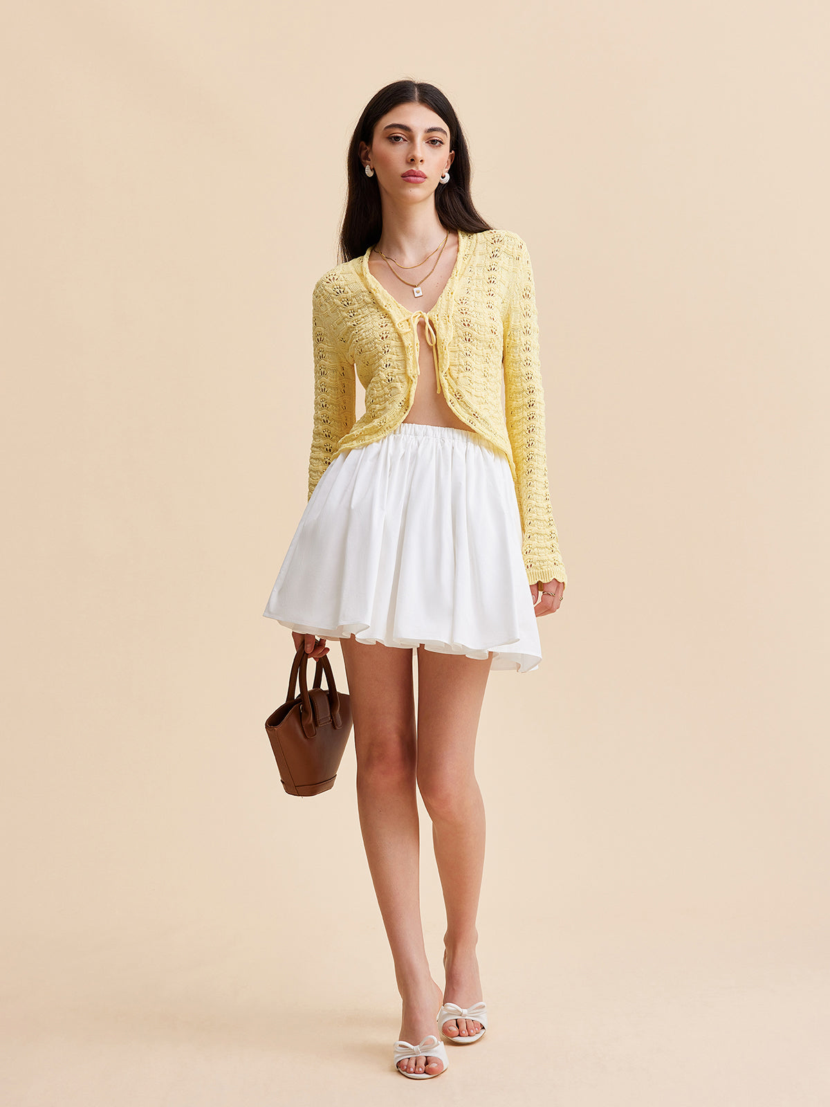 LA FINE FLEUR’s crocheted tie-front cardigan sweater over a nude top and white mini skirt.