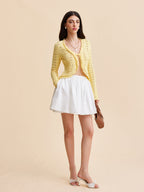 LA FINE FLEUR Crocheted Cardigan Sweater with tie-front over a light top, white skirt.