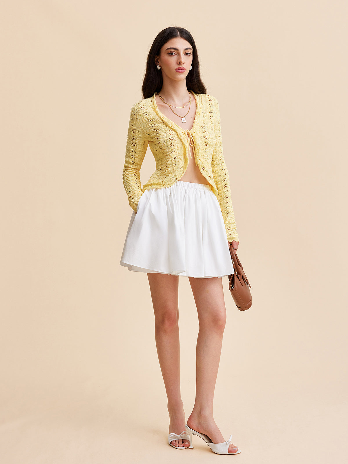 LA FINE FLEUR Crocheted Cardigan Sweater with tie-front over a light top, white skirt.