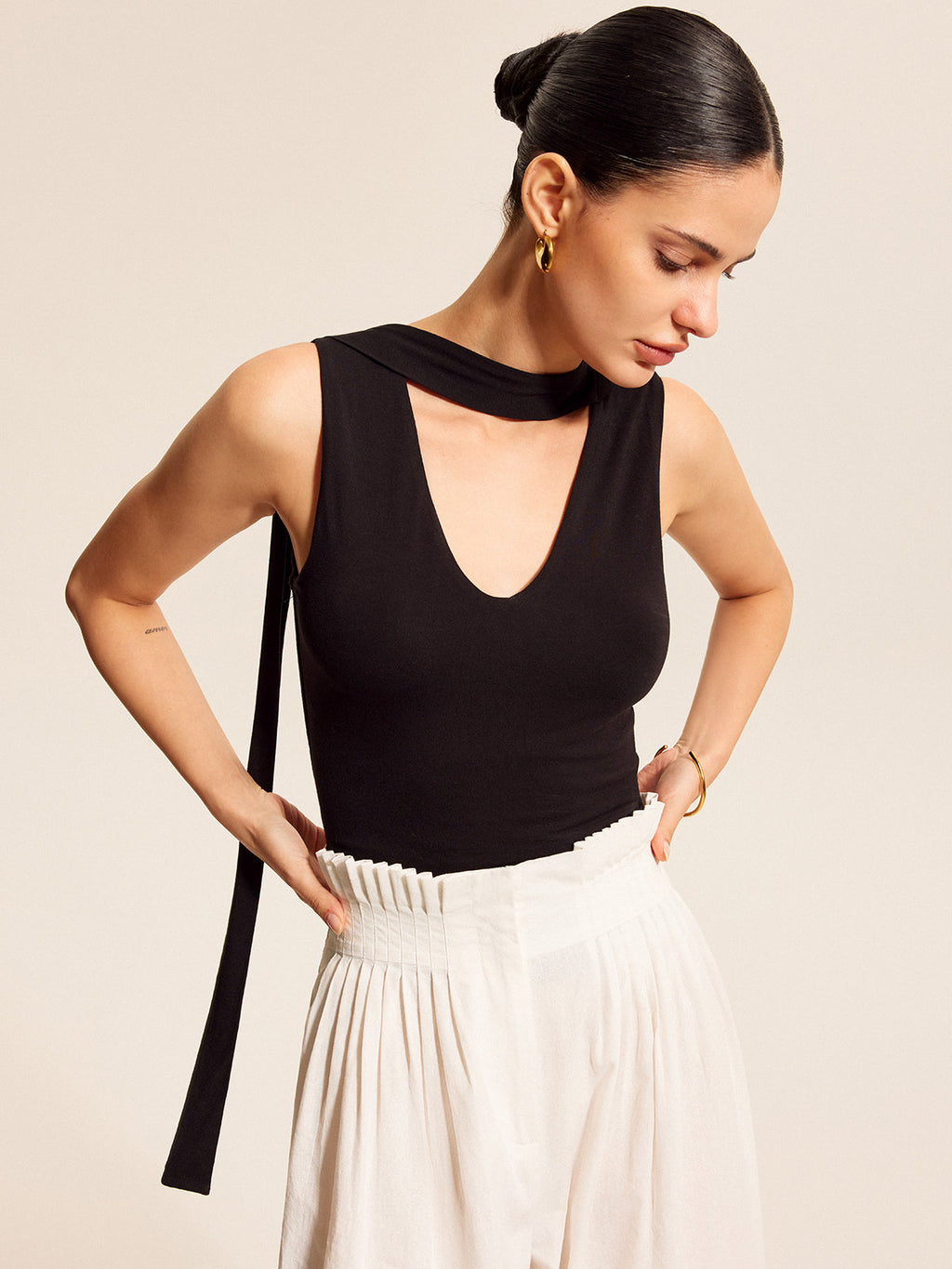 V-neck blouse with an elegant scarf-style neck tie and high-waisted, pleated white pants.