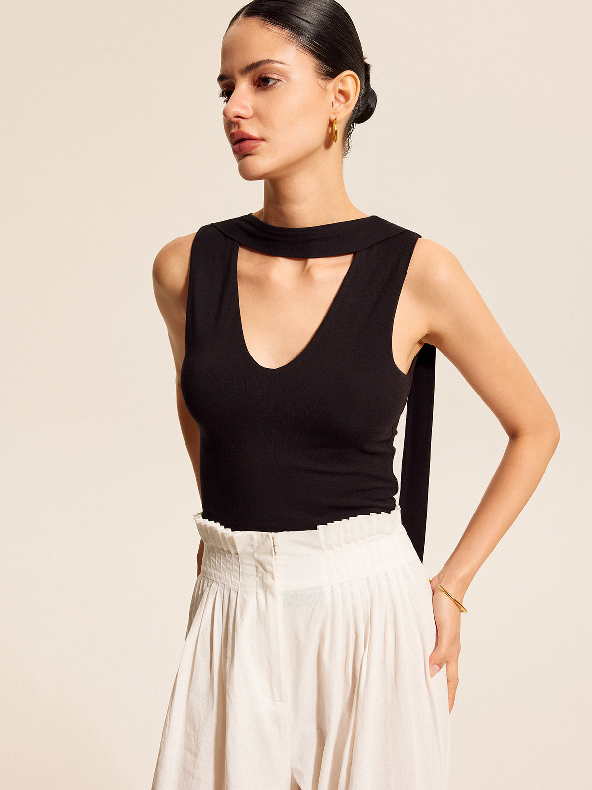 Sleeveless black V-neck blouse with an elegant scarf-style neck tie and white wide-leg pants.